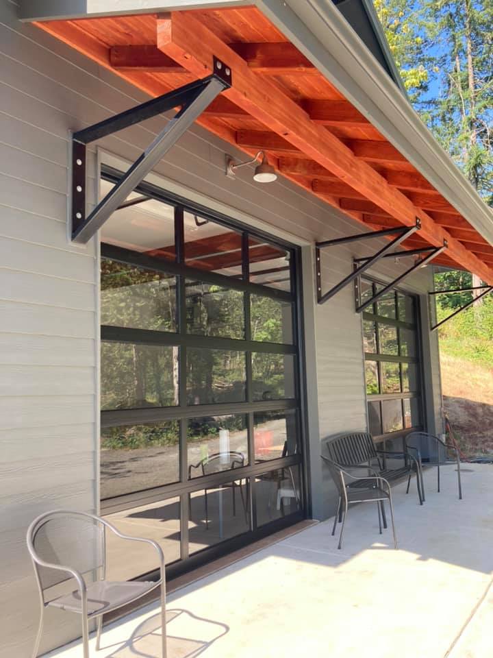 Custom garage build with modern glass panel doors, wood beam overhang, and outdoor seating area.