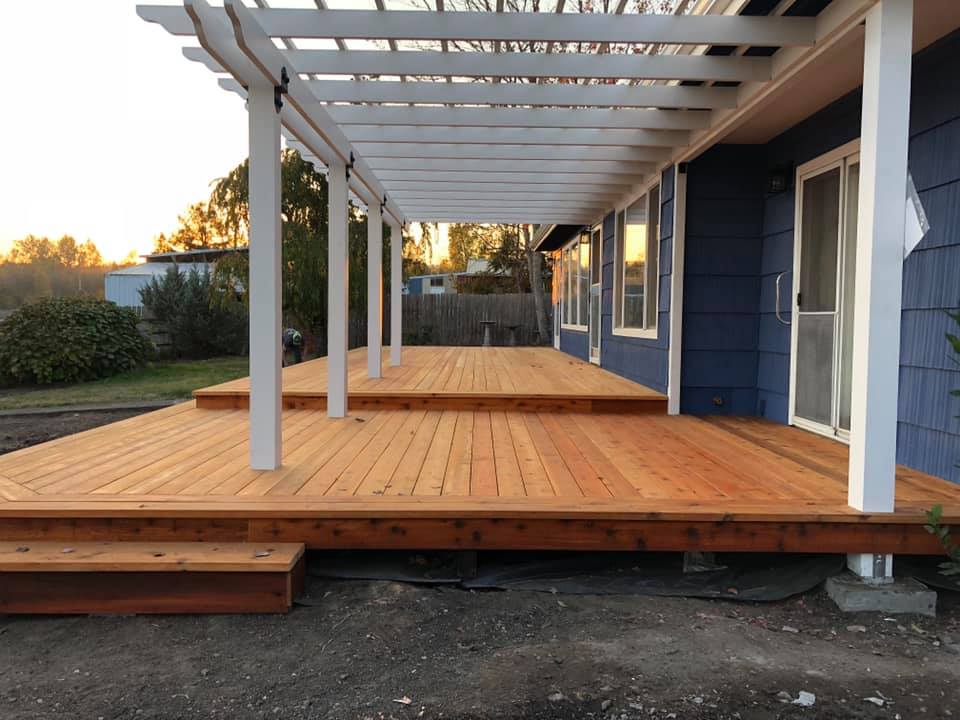 Custom wood deck with white pergola attached to home, featuring multi-level design for outdoor living space.
