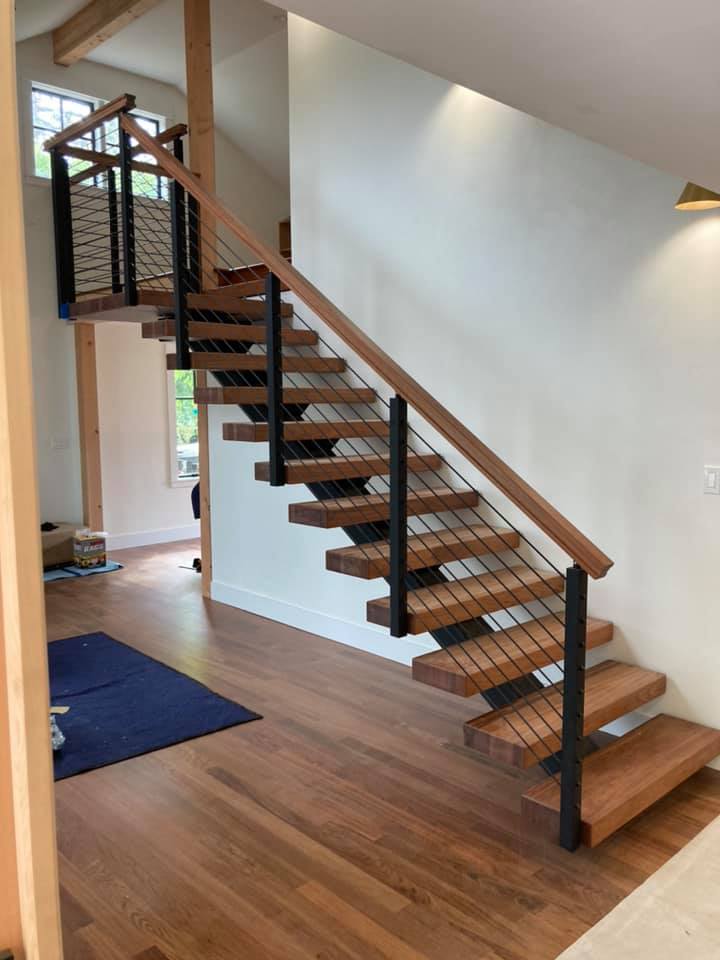 Modern floating staircase with wood treads and metal cable railing in custom home interior.
