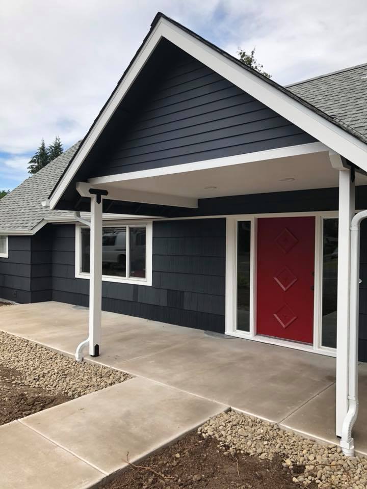 Custom home exterior remodel with black siding, covered porch, and red front door.
